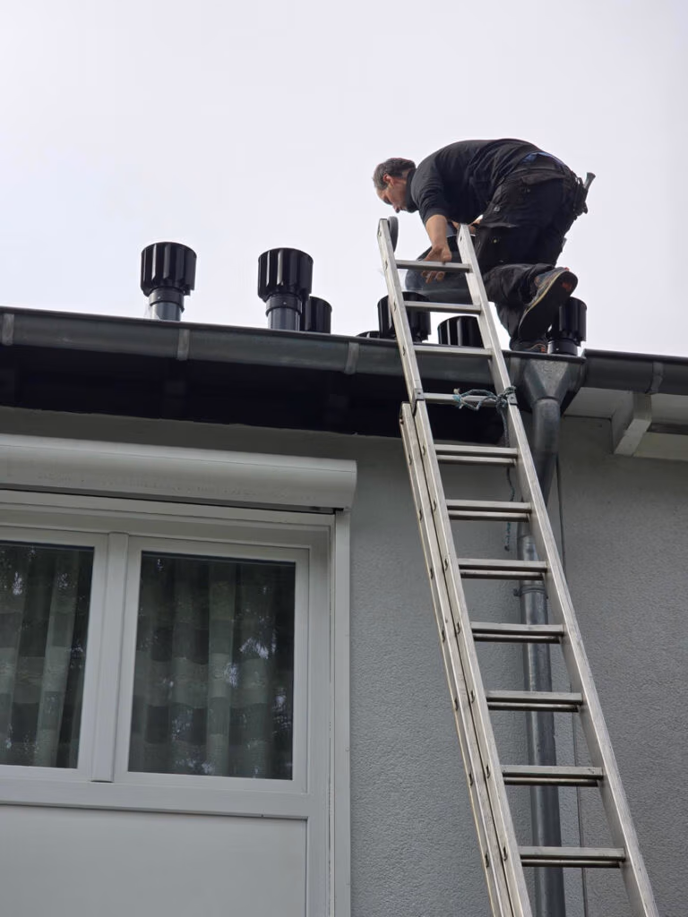 Georg Müller Dachdeckermeister installiert auf einem flach geneigten Pultdach die neuen Rotor-Zwangslüfter von Fleck GmbH. Die windgetriebenen Lüfter sollen die Entlüftung feuchteanfälliger Dachkonstruktionen verbessern. Foto: Verlag Bruchmann