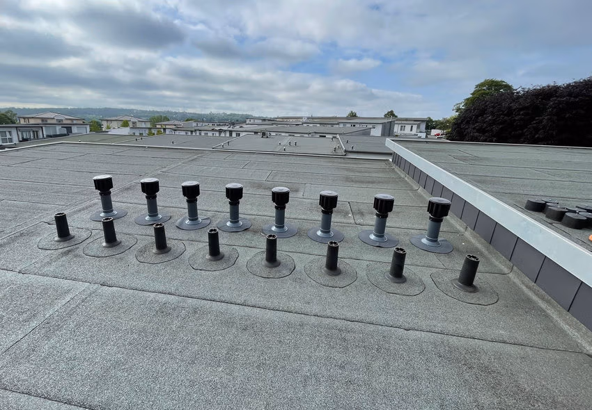 Vorher-Nachher-Vergleich auf dem fünf Grad geneigten Pultdach: Die bisherigen passiven Dachlüfter (vorn) werden schrittweise durch neue windgetriebene Rotor-Zwangslüfter von Fleck GmbH ersetzt. Die neuen Systeme sollen die aktive Entlüftung des Dachaufbaus verbessern und Feuchtigkeit effizienter abführen. Fotos: Verlag Bruchmann