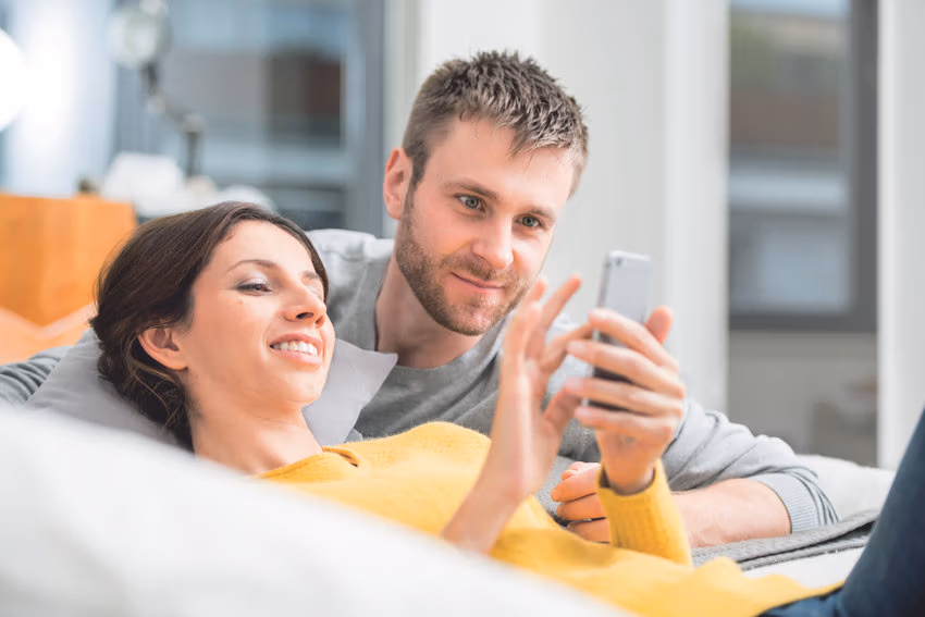 Ein Paar sitzt auf einem Sofa und betrachtet gemeinsam ein Smartphone.