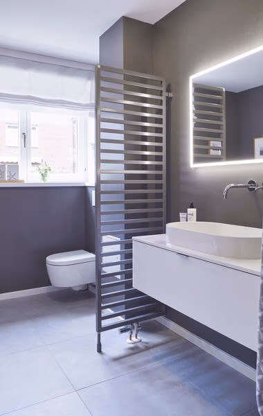 Geteilte Darstellung eines älteren und eines modernisierten Badezimmers mit blauem Badheizkörper.