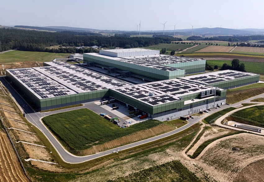 Schrägansicht des EDEKA-Logistikzentrums mit grünen Hallenfassaden, Lkw-Toren und Photovoltaikmodulen auf mehreren Dächern.