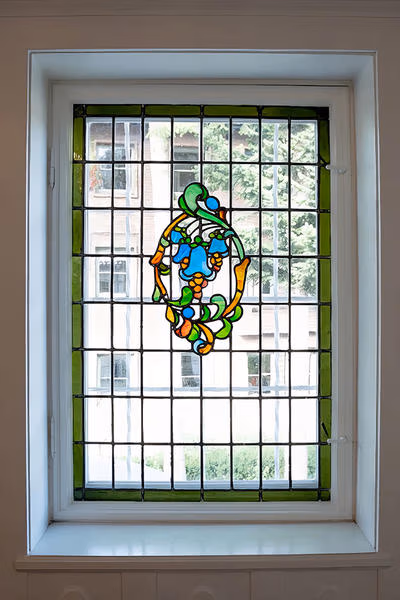 Fenster mit farbigem Bleiglas-Ornament und grünem Rahmen in einem historischen Gebäude.