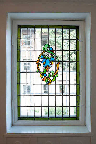 Fenster mit farbigem Bleiglas-Ornament und grünem Rahmen in einem historischen Gebäude.