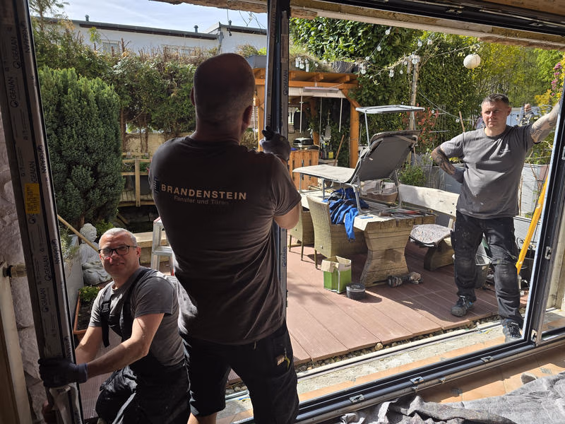 Drei Monteure beim Einbau einer Schiebetür zwischen Wohnraum und Terrasse.