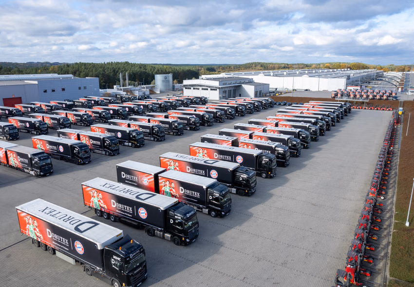 Reihen schwarzer Drutex-Lkw mit rot gestalteten Aufbauten vor Produktionshallen.