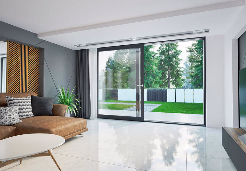 Drutex Iglo Edge Slide mit dunklen Rahmen als großflächiger Terrassenzugang in einem Wohnzimmer mit braunem Sofa.