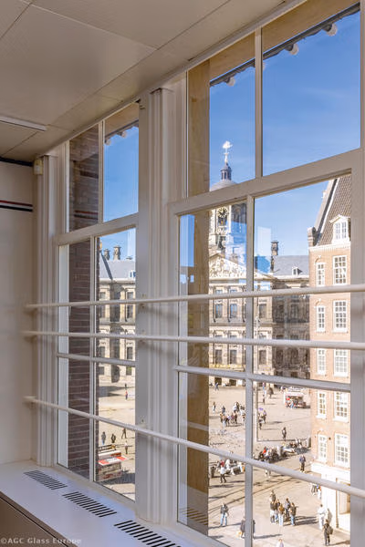 Hohe, weiß gerahmte Fenster mit horizontalen Schutzstangen und Blick auf den Dam-Platz