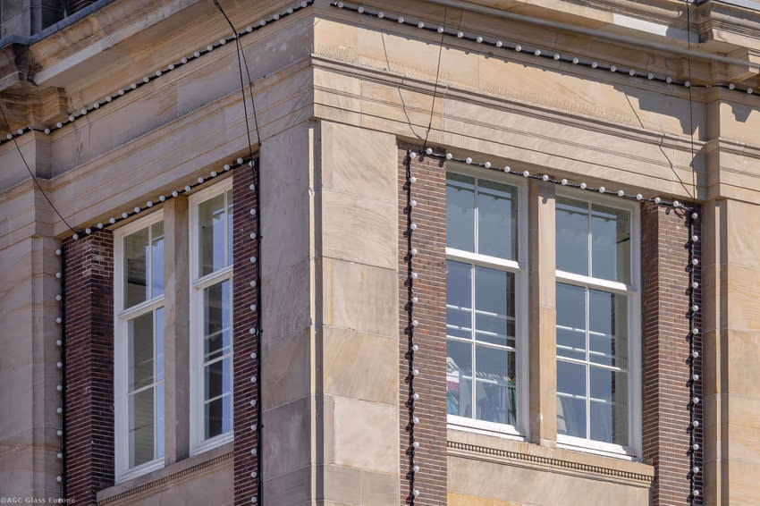 Weiße Fensterrahmen an einer Gebäudeecke mit Natursteinflächen und roten Ziegeln.