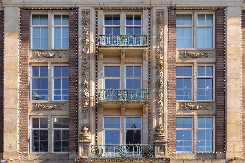 Drei Fensterachsen über mehrere Geschosse mit grünen Balkongeländern und Natursteindekor.