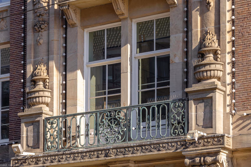 Schrägansicht eines Fensterpaars mit grünem Balkongeländer und verzierten Natursteinelementen.