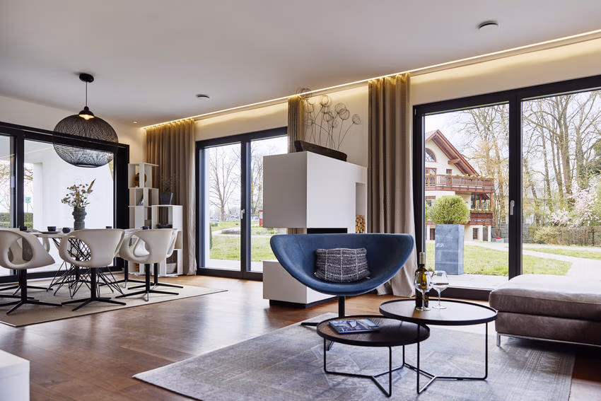 Offener Wohn- und Essbereich mit großen Fenstern, Esstisch, blauem Sessel und Sofa.