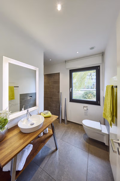 Badezimmer mit Aufsatzwaschbecken auf einer Holzplatte, beleuchtetem Spiegel, Dusche und WC.