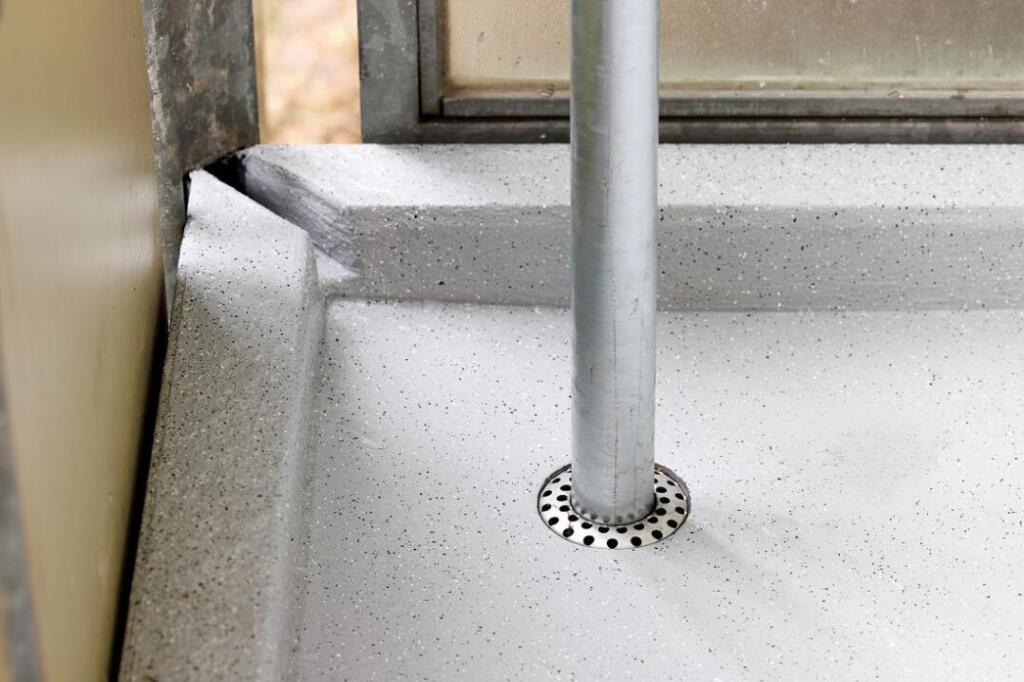 Die neue Hauptentwässerung:  Loro Serie GF, bei der das von oben kommende Rohr in den darunterliegenden Balkonablauf geführt wird. Über das Ringsieb fließt der Niederschlag in den Strang. Gut zu erkennen ist die Anstaufunktion in der Ecke, über die zuvor die gesamte Entwässerung erfolgte: Sollte ein extremer Regen dazu führen, dass die Wasserhöhe auf dem Balkon den Anstau an der Ecke übersteigt, übernimmt der alte Entwässerungsweg die Notentwässerung.