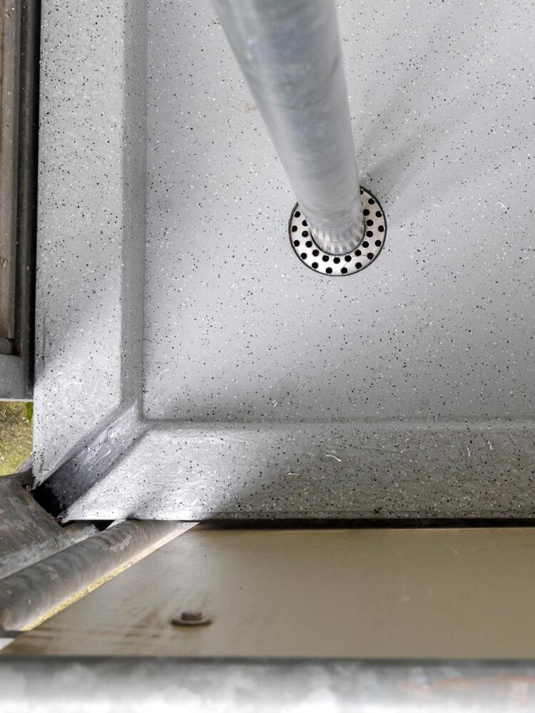 Die neue Hauptentwässerung:  Loro Serie GF, bei der das von oben kommende Rohr in den darunterliegenden Balkonablauf geführt wird. Über das Ringsieb fließt der Niederschlag in den Strang. Gut zu erkennen ist die Anstaufunktion in der Ecke, über die zuvor die gesamte Entwässerung erfolgte: Sollte ein extremer Regen dazu führen, dass die Wasserhöhe auf dem Balkon den Anstau an der Ecke übersteigt, übernimmt der alte Entwässerungsweg die Notentwässerung.